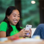 A smiling teenage girl wearing clear Invisalign aligners, holding her phone, showing the discreet and comfortable look of Invisalign Teen in Northwood, London.