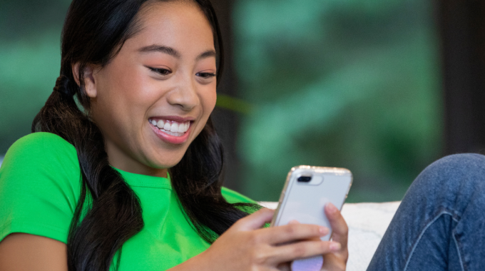 A smiling teenage girl wearing clear Invisalign aligners, holding her phone, showing the discreet and comfortable look of Invisalign Teen in Northwood, London.